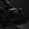 Predator Series boxing gloves in red accent being placed into a black gym bag in a locker room setting.