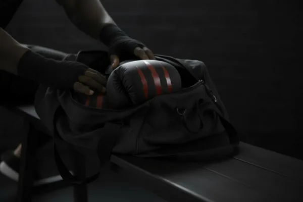 Predator Series boxing gloves in red accent being placed into a black gym bag in a locker room setting.
