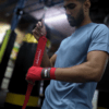 Boxer Moniah Miah wrapping hands with Animal Athletics Predator Series red hand wraps during training in a gym.