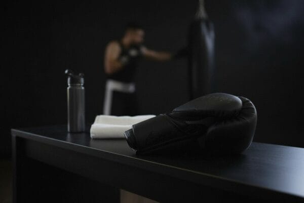 Predator Series black accent boxing glove on a gym bench with a boxer training in the background.