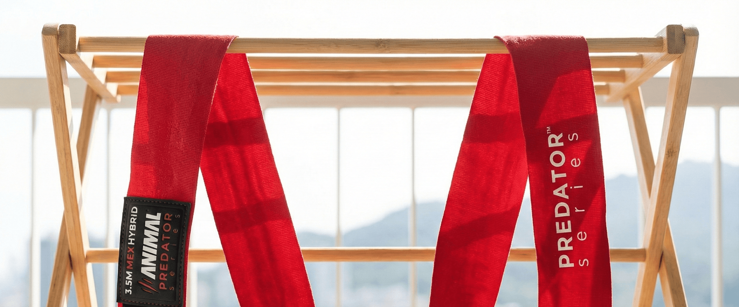 Red boxing hand wraps laid out flat on a clothes drying rack outdoors, air drying on an apartment balcony with buildings out of focus in the background.